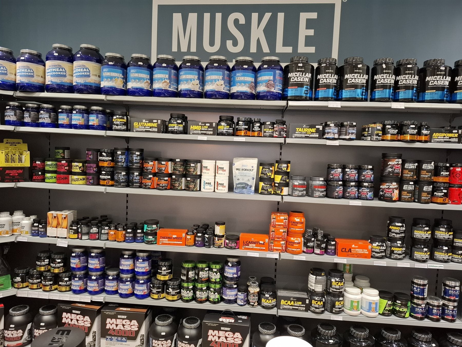 Pre-workoutwand van MUSKLE Antwerpen met performance-amino's onder het MUSKLE-bord