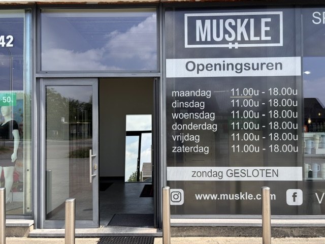 Ingang van MUSKLE Begijnendijk met openingsuren op de deur