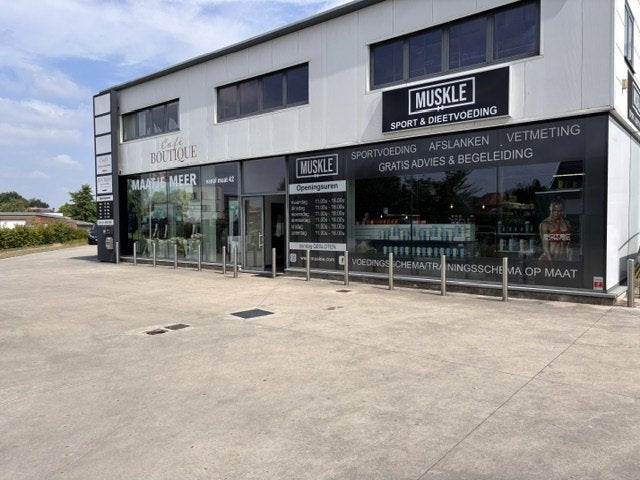 Voorgevel van MUSKLE Begijnendijk met MUSKLE-bord, openingsuren op het raam en parkeervoorterrein