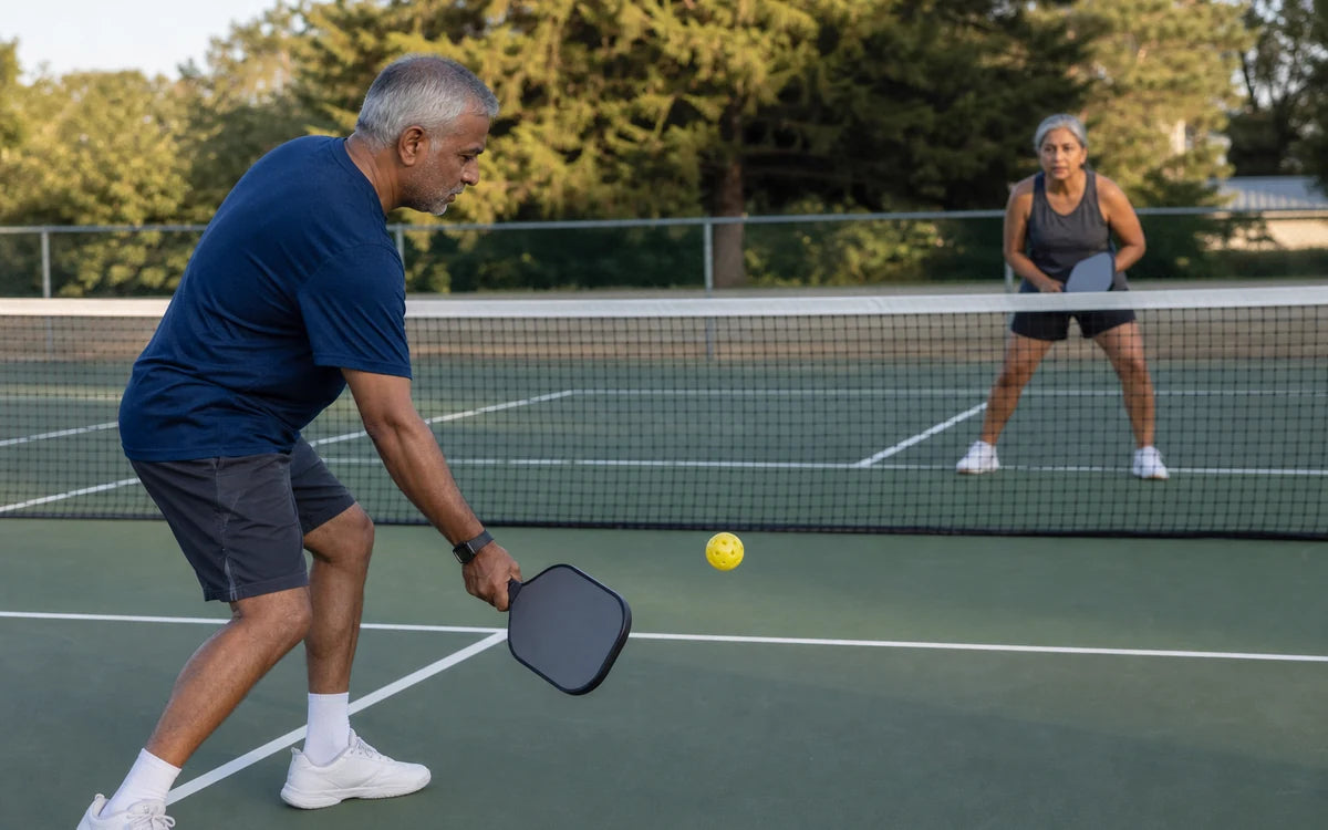Zuid-Aziatische man en mixed-race vrouw van 55 tot 65 jaar tijdens pickleball op een buitenbaan