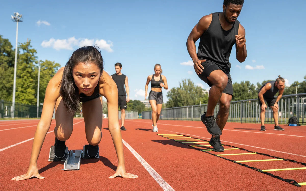 Diverse jongvolwassenen tijdens sprintstarts en agility drills op een atletiekbaan
