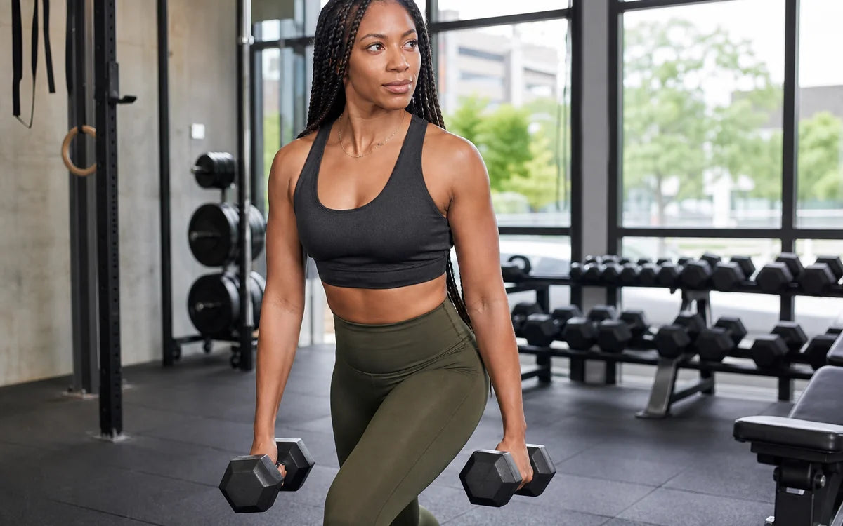Vrouw tijdens gecontroleerde krachttraining met dumbbells in een lichte moderne gym