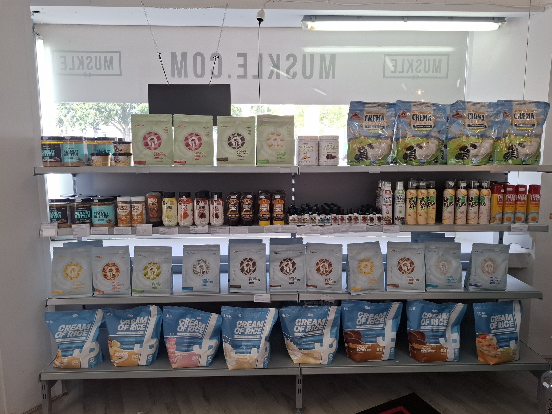 Shelves with whey, cream of rice and nutrition by the window at MUSKLE Roosendaal